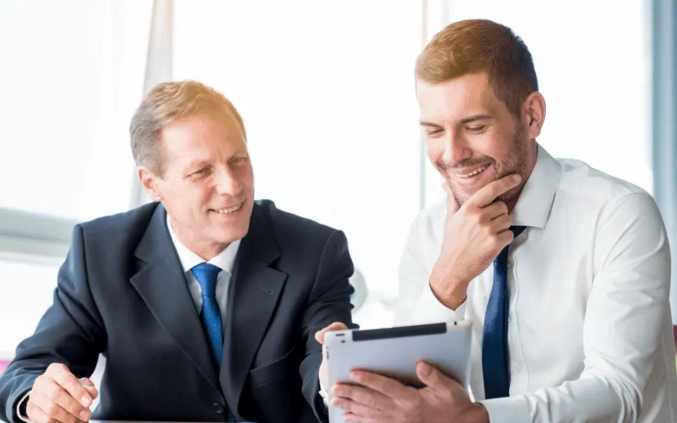 Attorney and client sitting at a desk discussing while the client looks amused viewing information on a tablet