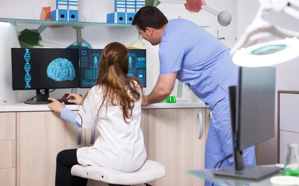 Senior doctor standing by desk reviewing imaging reports while female doctor observes attentively.