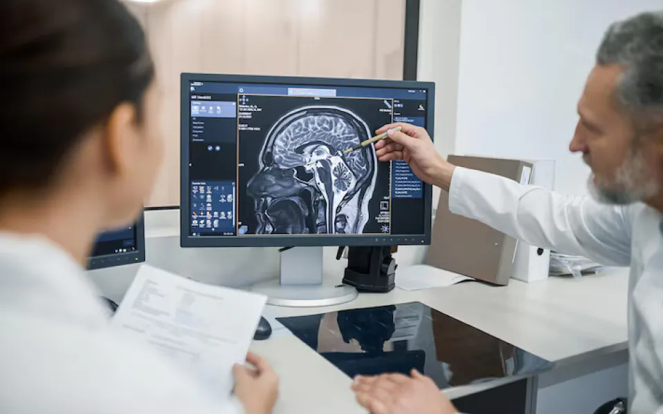 Doctor pointing at wall-mounted TV showing multiple head scans, emphasizing collaborative review.