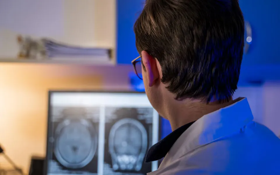Doctor pointing at a screen displaying CT scan images while talking with a patient