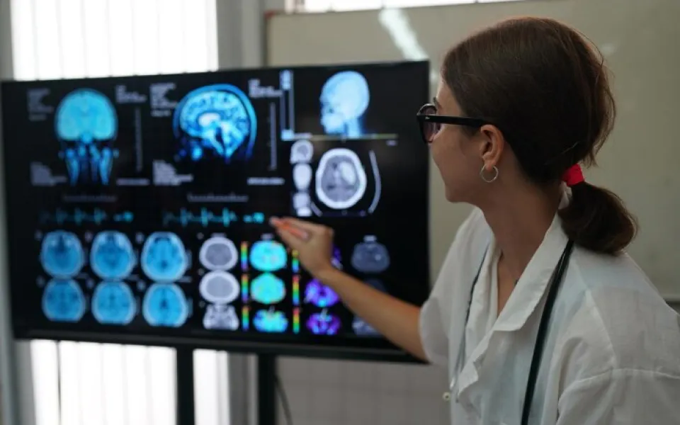 Young doctor pointing pen at TV screen showing medical imaging reports for detailed review.