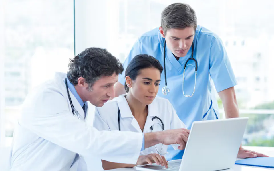 Two senior doctors and a junior doctor discussing patient imaging on laptop using Scriptoware’s remote platform.