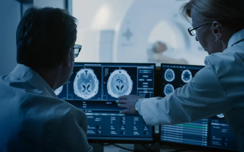 Senior female doctor talking with a male doctor while pointing at a screen displaying CT scan images