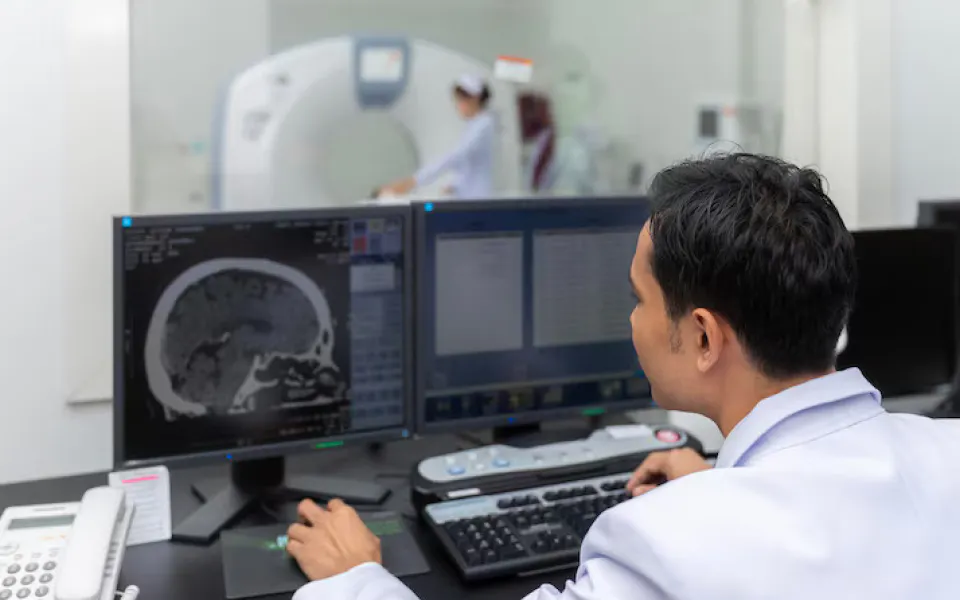 Doctor analyzing live MRI imaging reports while patient undergoes scan inside the MRI machine.