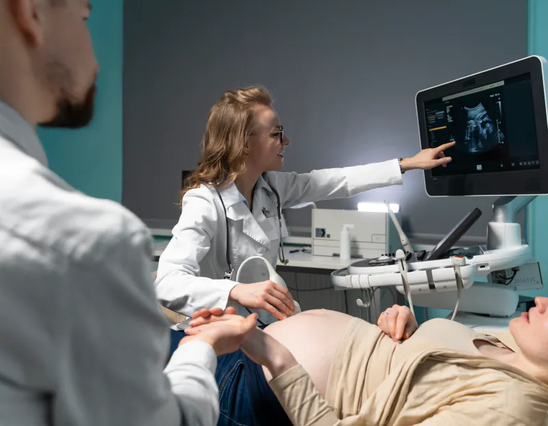 Doctor performing ultrasound on pregnant patient, pointing at live ultrasound screen.