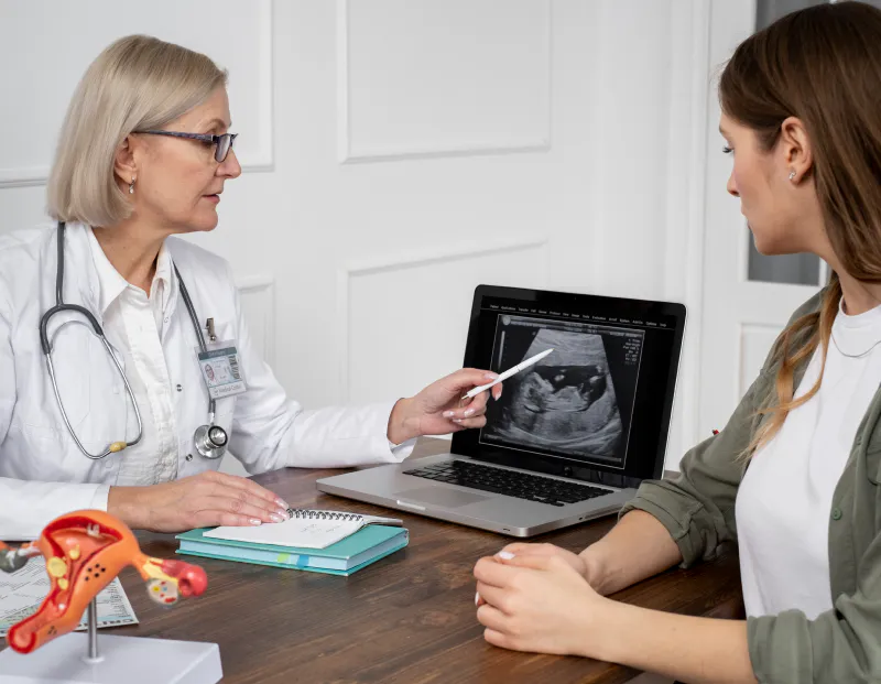 Doctor pointing at laptop displaying gynecological ultrasound report, discussing with patient.