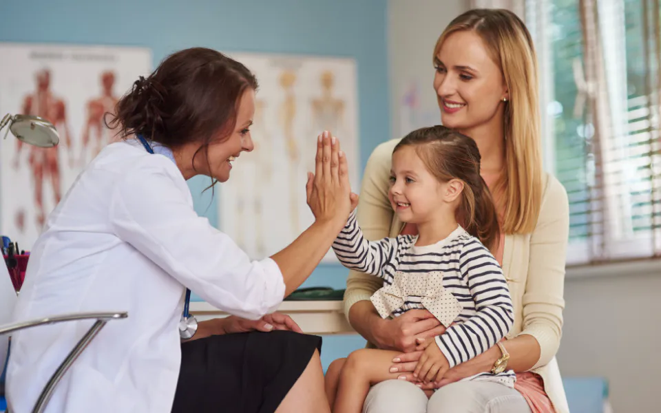 Female doctor giving hi-five to child on mother’s lap, promoting patient control with Scriptoware dashboard.