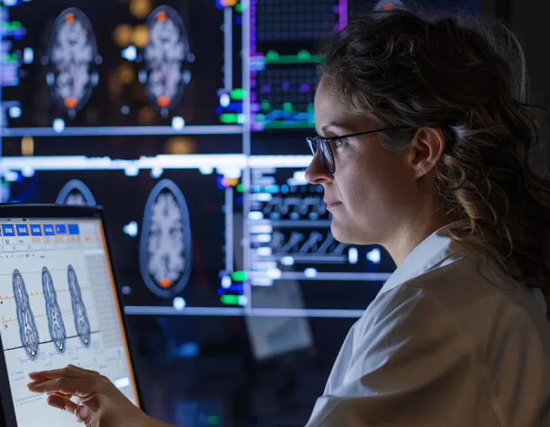 Doctor carefully reviewing multiple tumor scan reports on monitor in clinical setting.