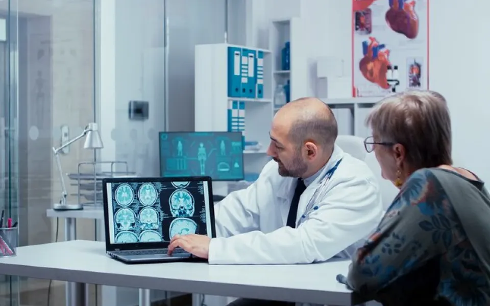 Doctor pointing at laptop screen displaying brain scan while discussing with patient